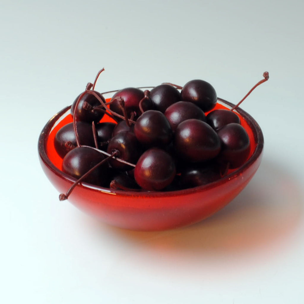 a red bowl filled with cherries on top of a white table