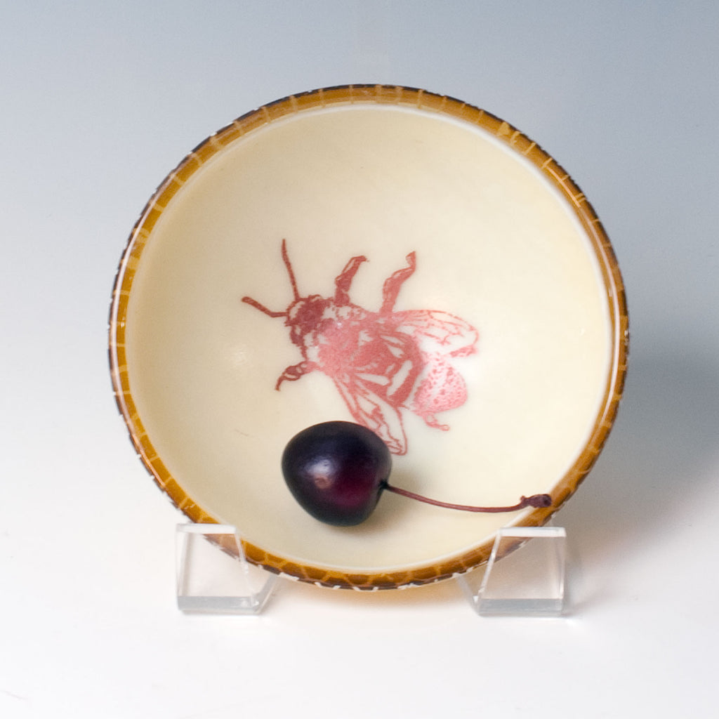 a bowl with a bee on it and a cherry in it