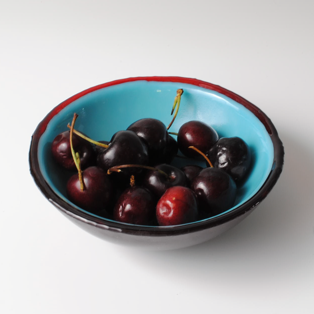 a blue bowl filled with cherries on top of a white table