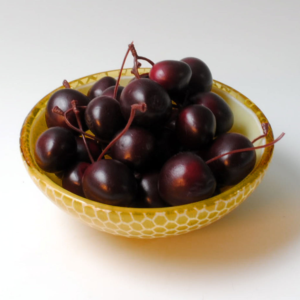 a yellow bowl filled with black cherries on a white table