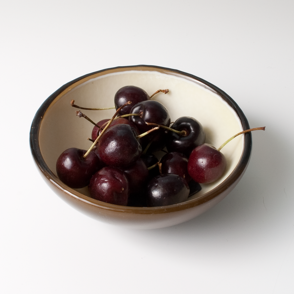 a bowl of cherries on a white surface