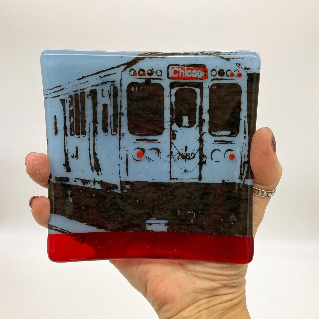 a hand holding a glass coaster with a train on it